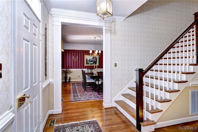 foyer entrance featuring a notable chandelier, wood finished floors, stairway, wallpapered walls, and baseboards