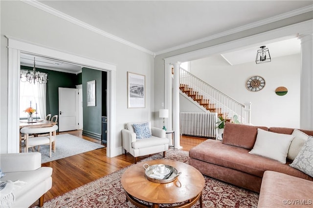 living area with stairs, wood finished floors, ornamental molding, and ornate columns