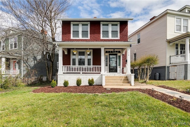 american foursquare style home featuring a porch, brick siding, and a front yard