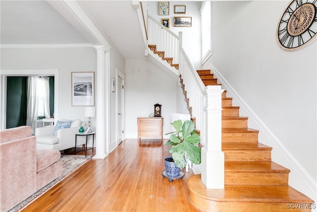 staircase featuring a wealth of natural light, wood finished floors, ornamental molding, and ornate columns