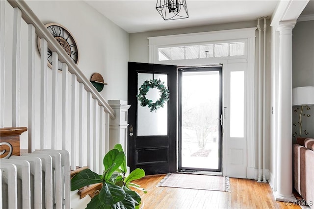 foyer entrance featuring light wood finished floors, stairs, radiator heating unit, and decorative columns