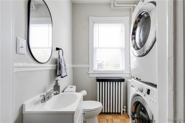 bathroom with toilet, radiator, vanity, and stacked washer / drying machine