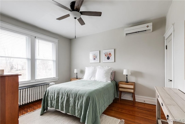 bedroom with radiator, baseboards, a wall unit AC, and wood finished floors