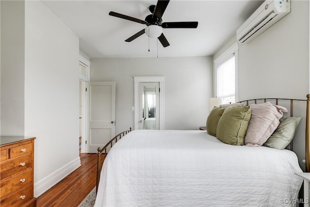 bedroom with ceiling fan, baseboards, an AC wall unit, and wood finished floors