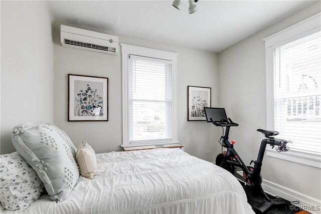 bedroom featuring multiple windows, a wall mounted AC, and baseboards