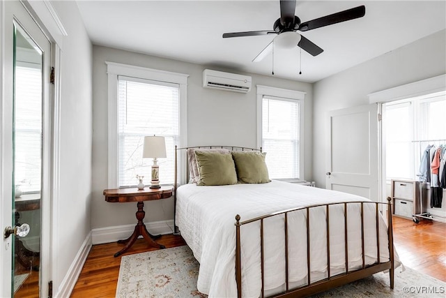 bedroom featuring ceiling fan, baseboards, light wood-style flooring, and a wall unit AC