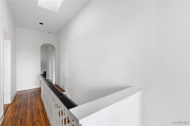 hall with baseboards, arched walkways, a skylight, an upstairs landing, and dark wood-style floors