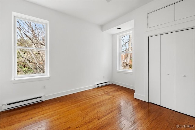 unfurnished bedroom featuring a baseboard heating unit, a closet, wood finished floors, and baseboards