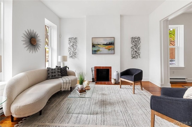 living area with baseboards, wood finished floors, a tile fireplace, and a baseboard radiator