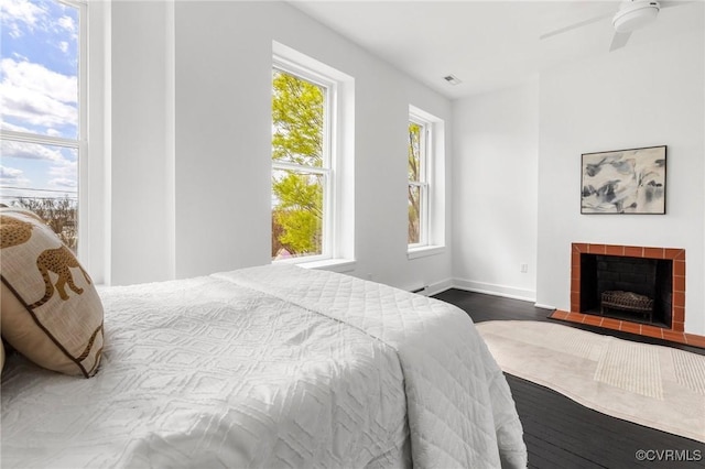 bedroom featuring ceiling fan, visible vents, baseboards, a tile fireplace, and wood finished floors