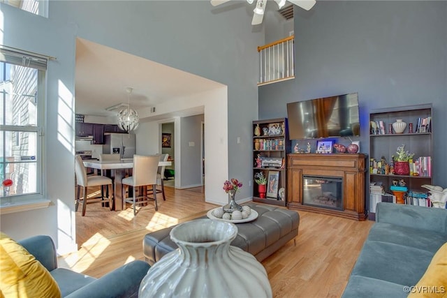 living room featuring a wealth of natural light, light wood-style floors, a high ceiling, and a glass covered fireplace