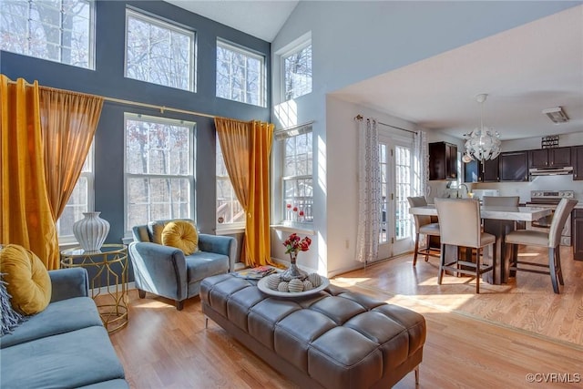 living room with an inviting chandelier, a towering ceiling, baseboards, and light wood finished floors