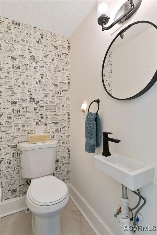 half bath featuring a sink, baseboards, toilet, and tile patterned flooring