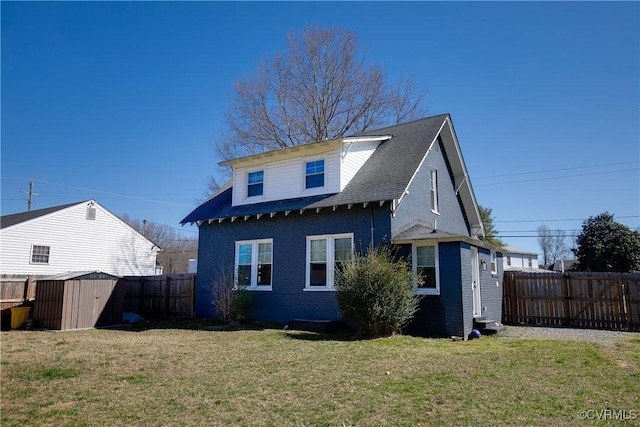 back of house featuring a storage unit, a lawn, a fenced backyard, and brick siding