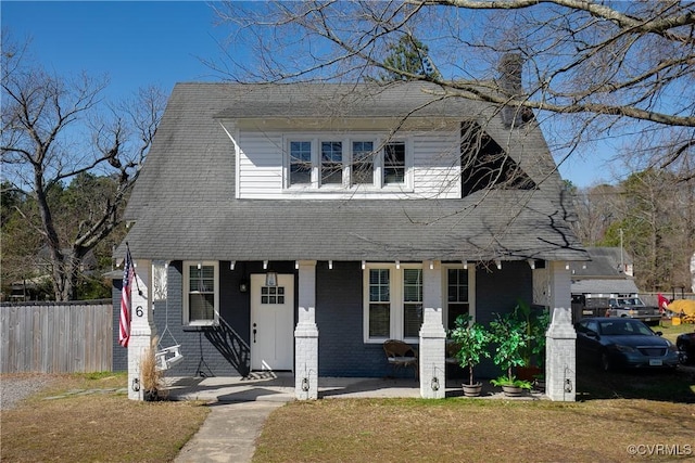 view of front facade featuring a front lawn, fence, roof with shingles, brick siding, and a chimney