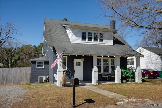 view of front of property with a porch, fence, a front yard, central AC unit, and a chimney