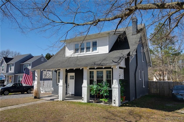 view of front of property with fence, roof with shingles, a front yard, brick siding, and a chimney