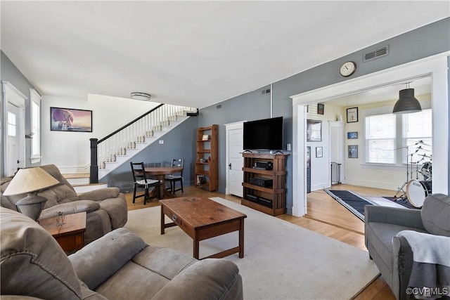 living room featuring stairs, baseboards, visible vents, and light wood-type flooring