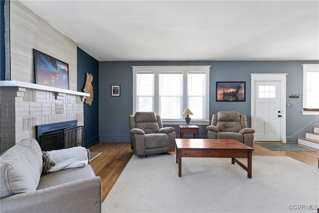 living area featuring stairway, a fireplace, baseboards, and wood finished floors