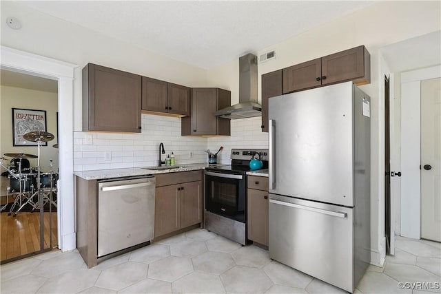 kitchen featuring backsplash, wall chimney range hood, light stone countertops, appliances with stainless steel finishes, and a sink