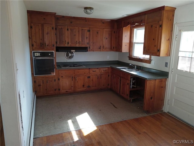 kitchen with a sink, black oven, dark countertops, and brown cabinetry