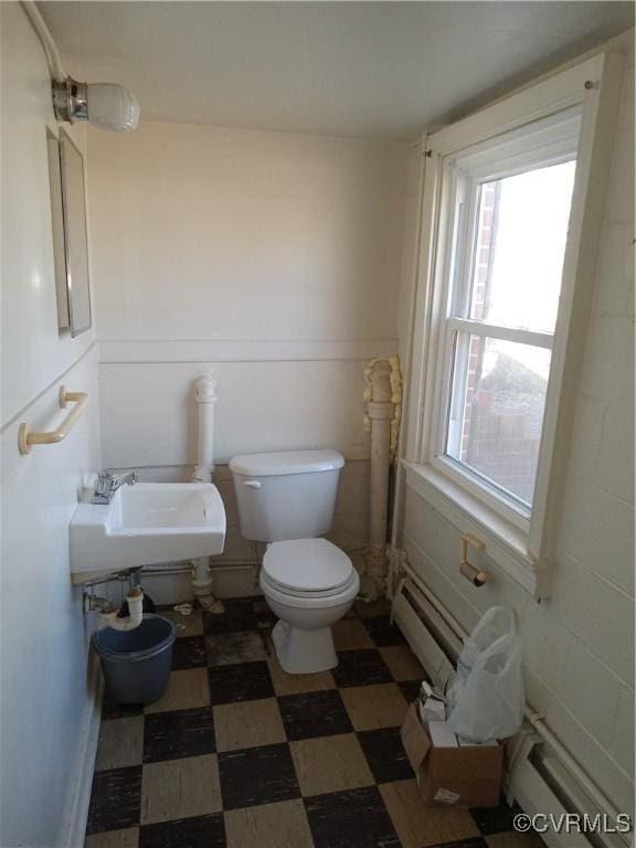 half bathroom featuring tile patterned floors, toilet, a baseboard radiator, and a sink