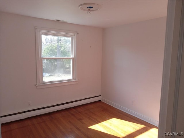 spare room featuring visible vents, wood finished floors, baseboards, and a baseboard radiator