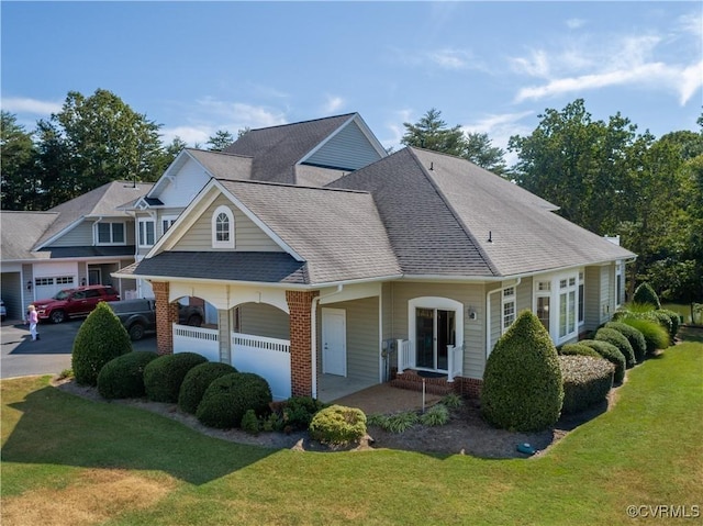 view of front of house featuring a front lawn, a garage, brick siding, and roof with shingles