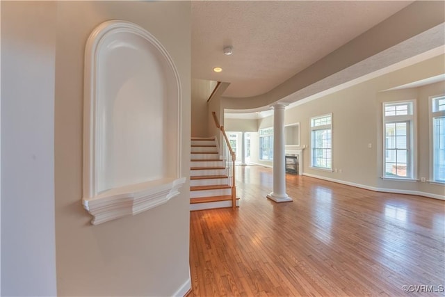 spare room with a wealth of natural light, stairway, light wood-type flooring, and ornate columns