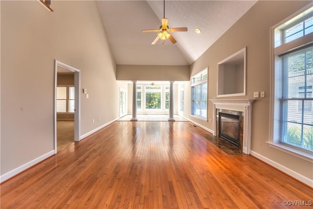 unfurnished living room with a wealth of natural light, a ceiling fan, wood finished floors, a premium fireplace, and ornate columns