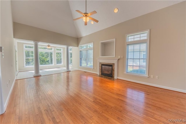 unfurnished living room with ceiling fan, decorative columns, light wood-style flooring, a fireplace, and high vaulted ceiling