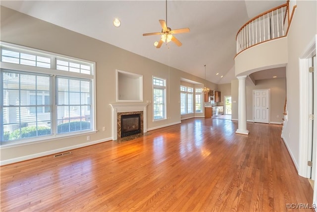 unfurnished living room featuring light wood finished floors, visible vents, high vaulted ceiling, and ornate columns