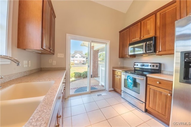 kitchen with light tile patterned flooring, a sink, stainless steel appliances, light countertops, and brown cabinets