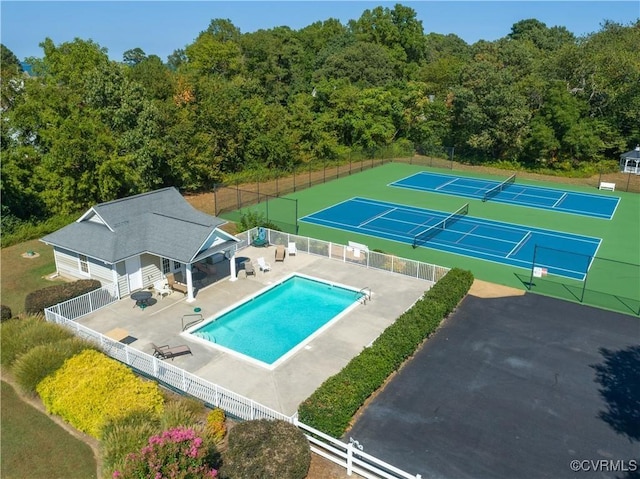 community pool with a patio area, a tennis court, and fence