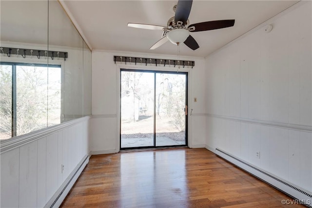 empty room featuring baseboard heating, a healthy amount of sunlight, crown molding, and wood finished floors