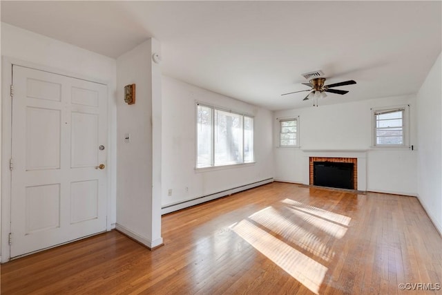 unfurnished living room with light wood finished floors, visible vents, a healthy amount of sunlight, a brick fireplace, and a baseboard radiator