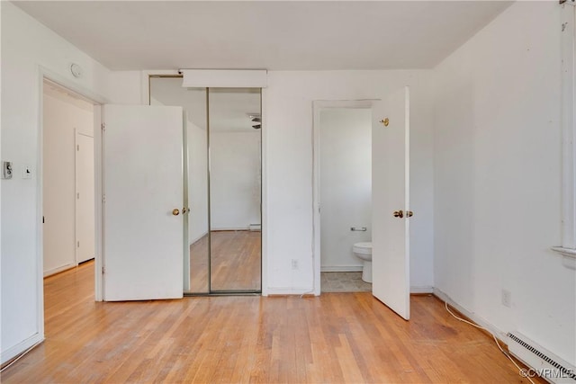 unfurnished bedroom with baseboards, baseboard heating, ensuite bathroom, wood finished floors, and a closet