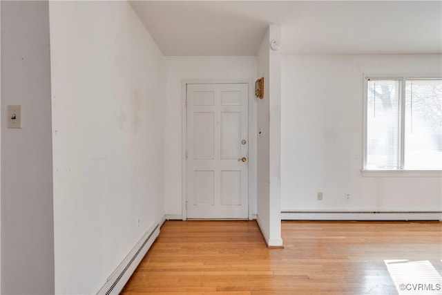 empty room with a baseboard radiator, baseboards, light wood-style flooring, and a baseboard heating unit