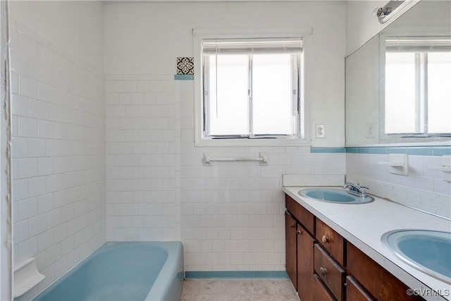 full bath featuring double vanity, a healthy amount of sunlight, tile walls, and a sink