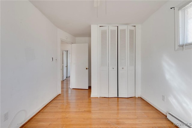 unfurnished bedroom featuring a closet, baseboard heating, baseboards, and light wood-style floors