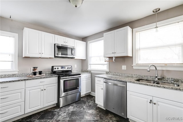 kitchen with a sink, stainless steel appliances, light stone counters, and white cabinetry