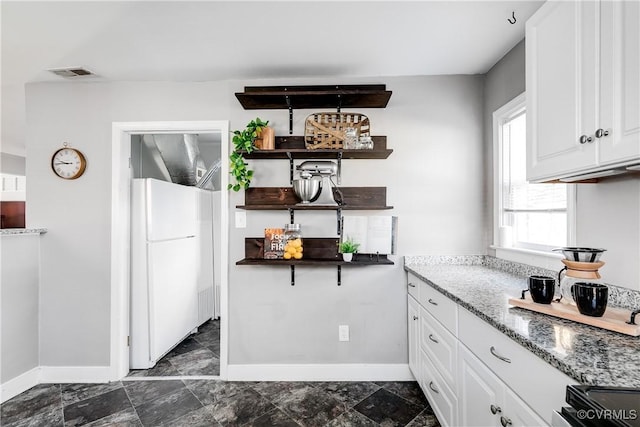 kitchen featuring visible vents, freestanding refrigerator, white cabinets, stone counters, and baseboards