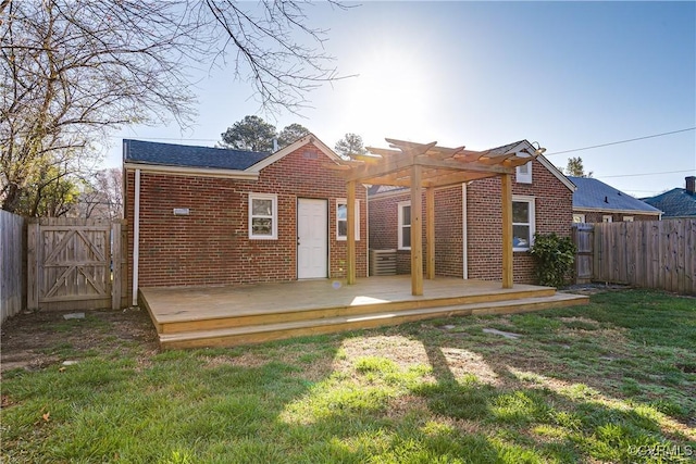 back of property with brick siding, a lawn, a fenced backyard, a deck, and a pergola