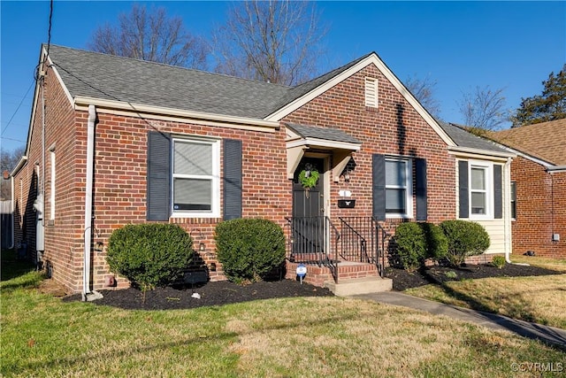 view of front of home featuring a front yard, brick siding, and a shingled roof