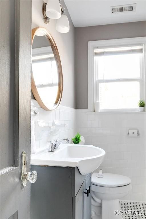 bathroom with vanity, a wainscoted wall, visible vents, tile walls, and toilet