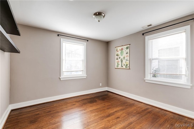 spare room featuring visible vents, dark wood-type flooring, and baseboards