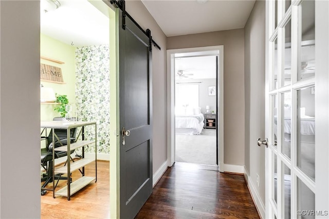 corridor featuring a barn door, baseboards, and wood finished floors