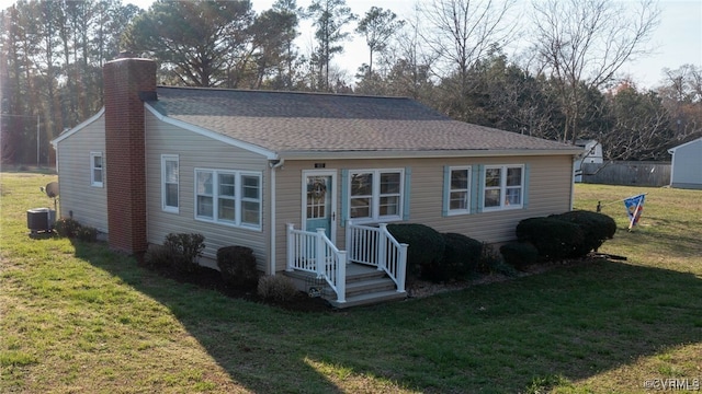 back of house with a shingled roof, a yard, central AC, and a chimney