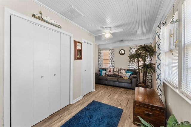 interior space with visible vents, a ceiling fan, light wood-style flooring, and crown molding