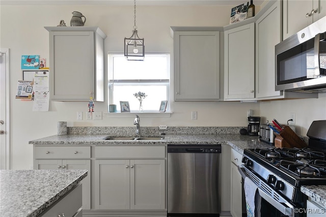 kitchen featuring a sink, light stone counters, appliances with stainless steel finishes, and hanging light fixtures